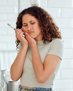 Woman in white bathroom holding hand to face in pain