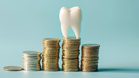 Model tooth on top of a pile of coins with light teal background