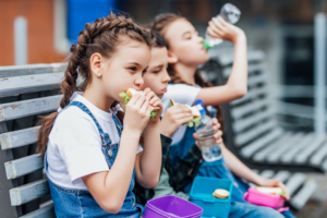 Three girls sitting on a school bench eating their lunches